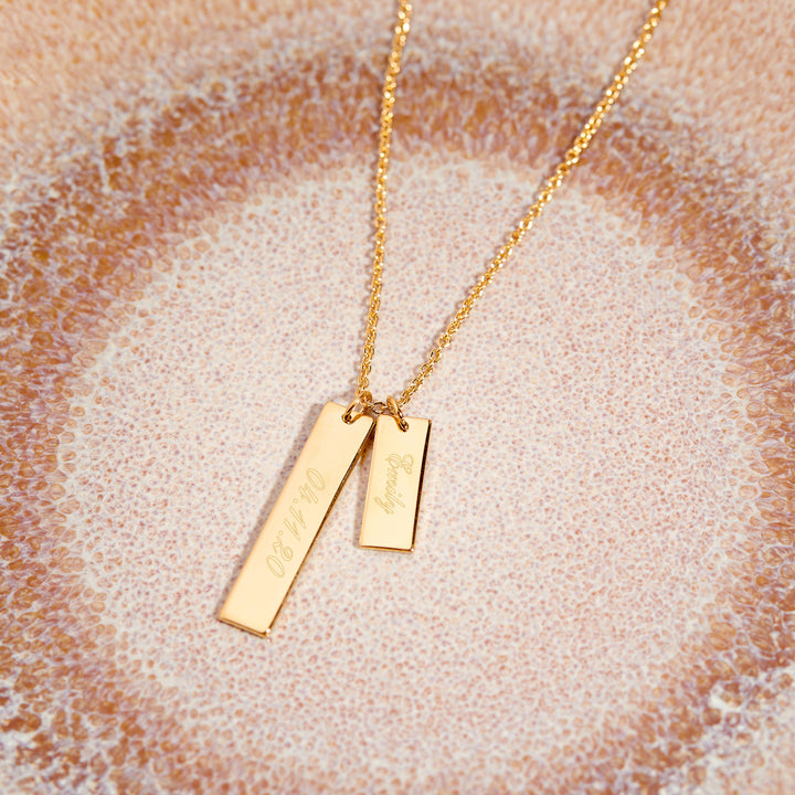 Gold necklace with two rectangular pendants on a textured beige background