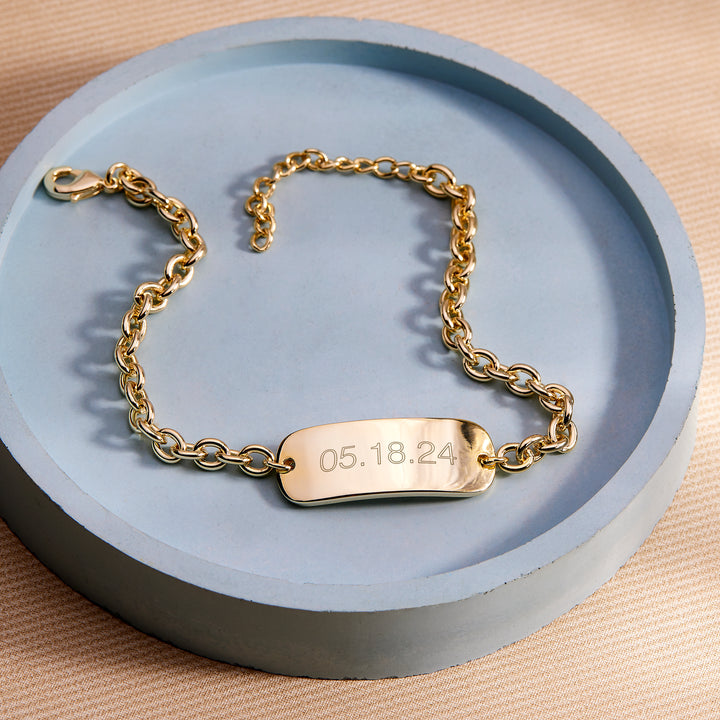 Gold chain bracelet with a engraved date tag on a blue dish