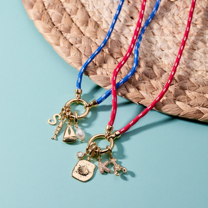 Two necklaces with charms on blue and red cords against a straw mat background
