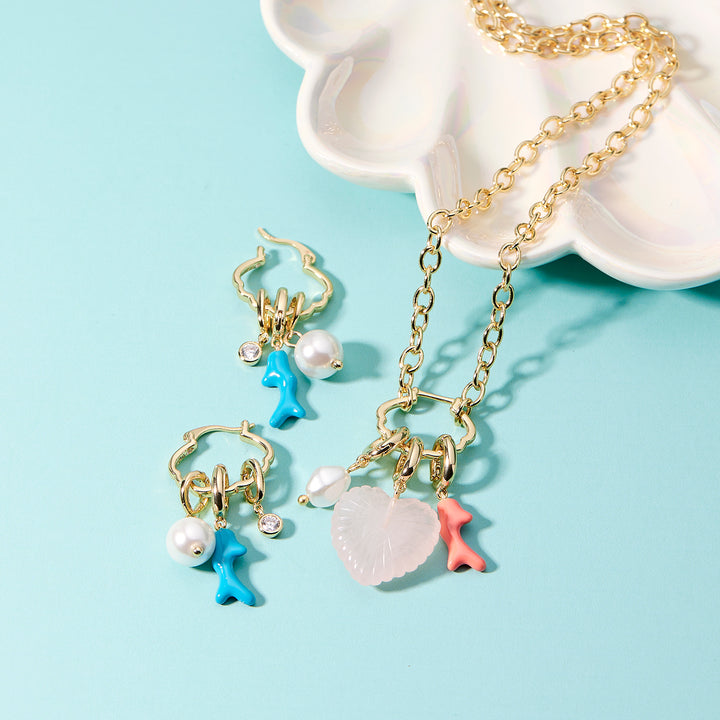 Jewelry set with gold chain necklace, earrings, and pendants on a light blue background
