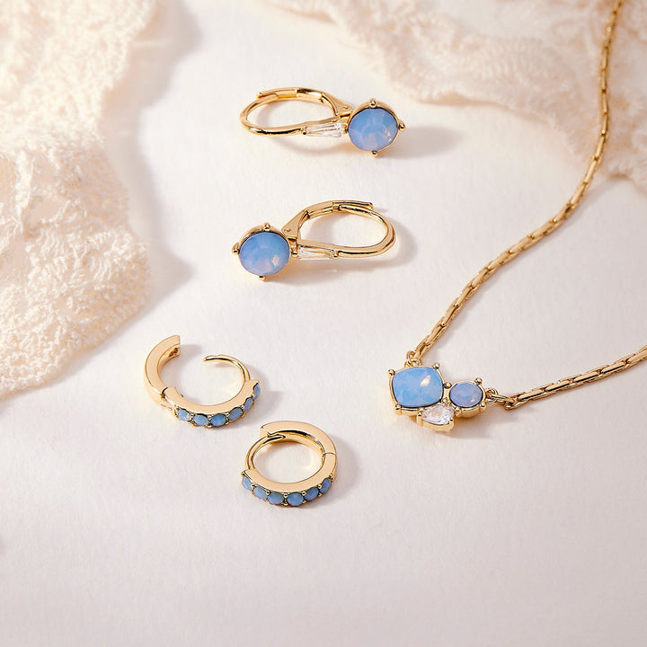 Gold jewelry set with blue stones on a textured white surface