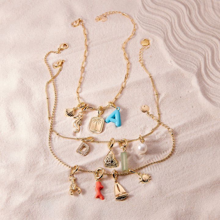 Gold necklace with various charms on a textured beige surface