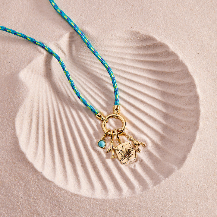 Necklace with gold charm and blue beads on a shell-shaped sand background