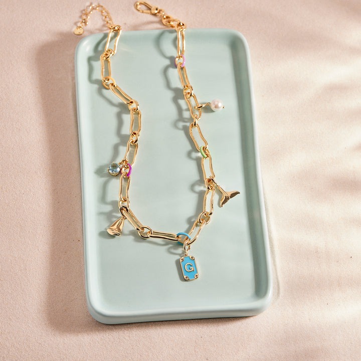 Gold necklace with a blue pendant on a light green tray against a beige background