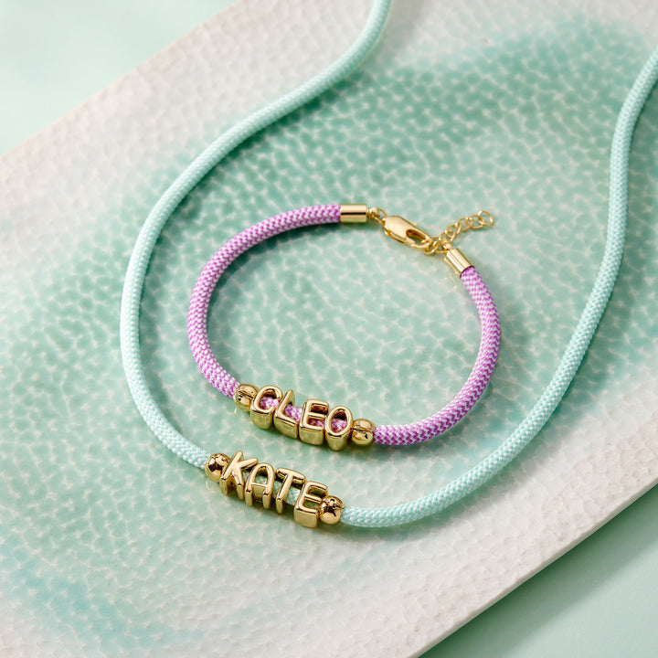 Bracelet with gold name charms on a light green fabric background