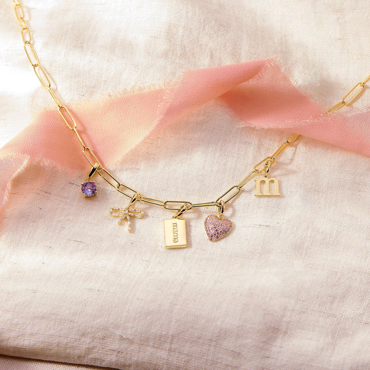 Gold necklace with various charms on a soft pink fabric background
