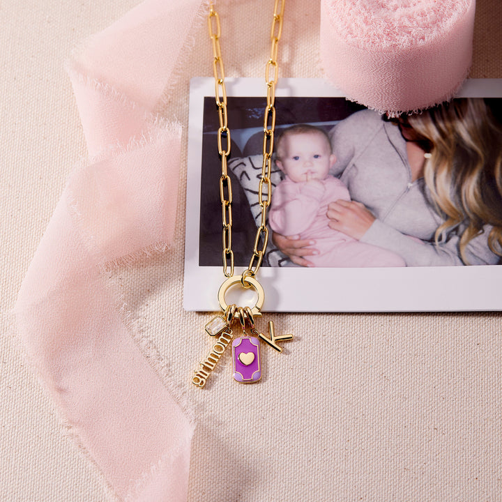Gold necklace with charms on a pink fabric background with a photo of a baby and woman.