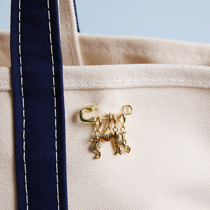 Gold charm set on a beige tote bag with a blue strap.