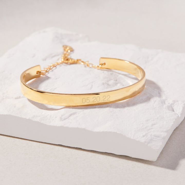 Gold bracelet with engraved date on a white fabric background