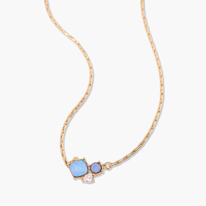 Gold necklace with blue gemstones and a pearl on a white background