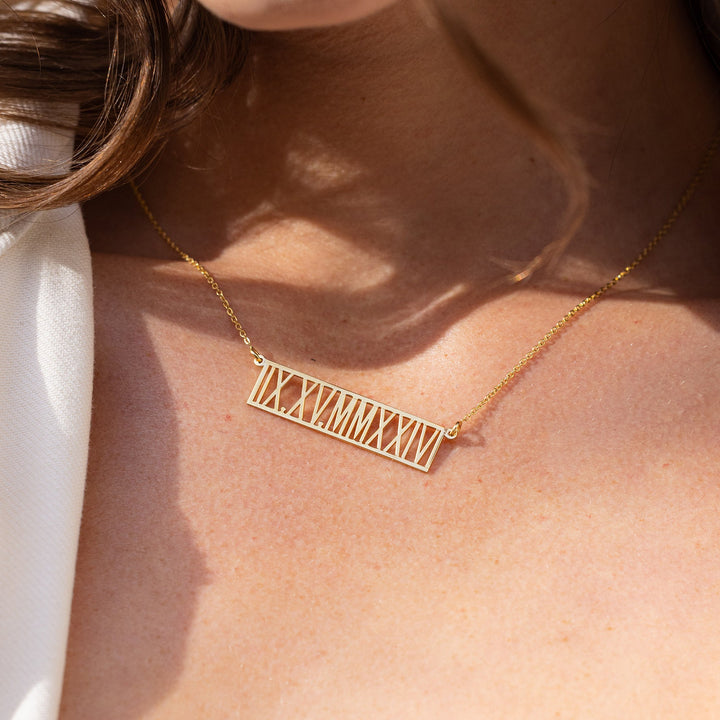 Close-up of a person wearing a gold necklace with engraved text, against a blurred background.