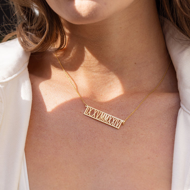 Close-up of a person wearing a gold necklace with a nameplate.