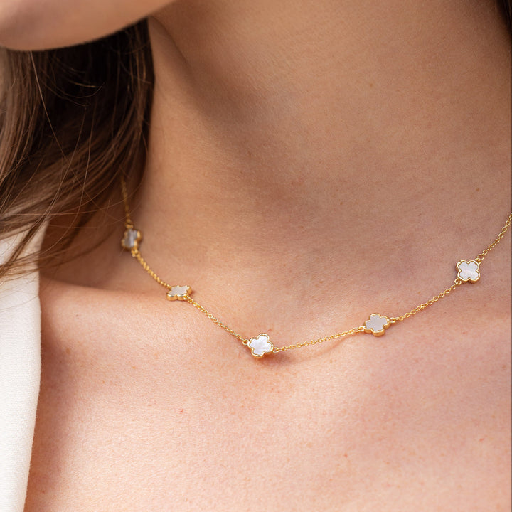 Gold necklace with small pendants on a person wearing a white top.