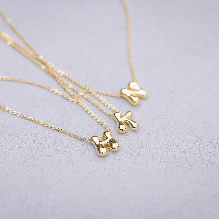 Three gold necklaces with small pendant designs on a light gray background