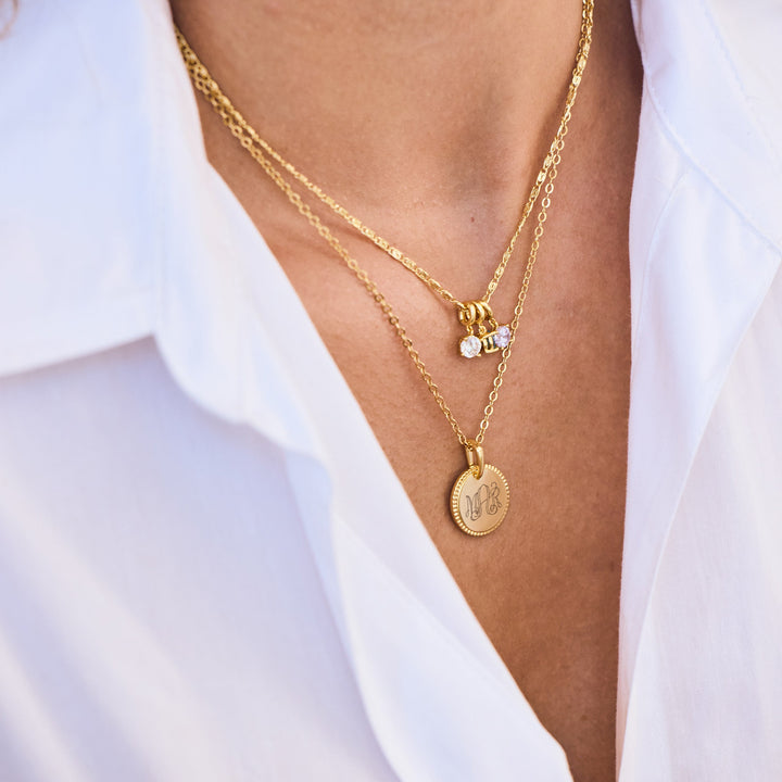 Gold necklaces with pendants on a person wearing a white shirt.