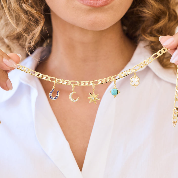 Gold chain necklace with charms held by a person wearing a white shirt