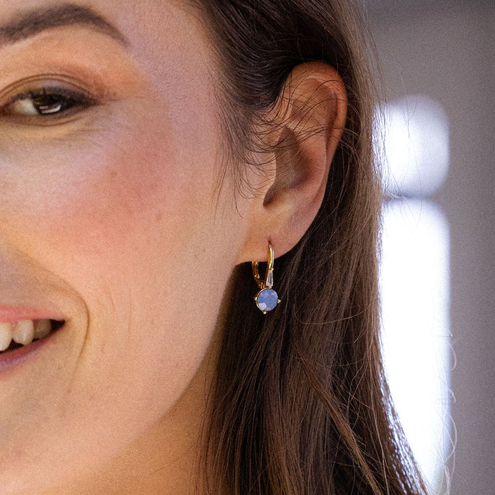 Close-up of a woman wearing a gold earring with a blue gemstone.