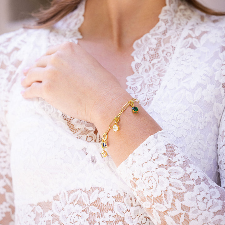 Close-up of a person wearing a gold bracelet with green gemstones on a white lace garment.