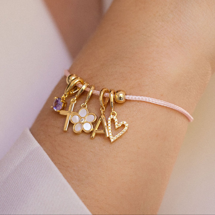 Gold bracelet with charms on a wrist against a neutral background