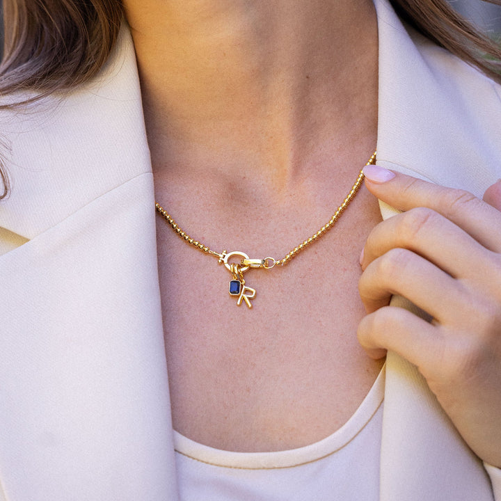 Woman wearing a gold necklace with a small pendant outdoors
