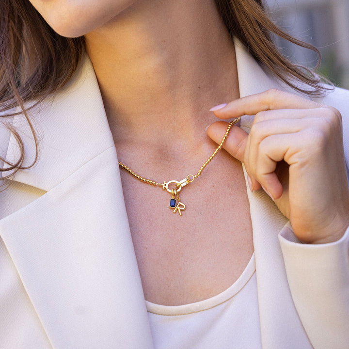 Woman wearing a gold necklace with a small pendant outdoors