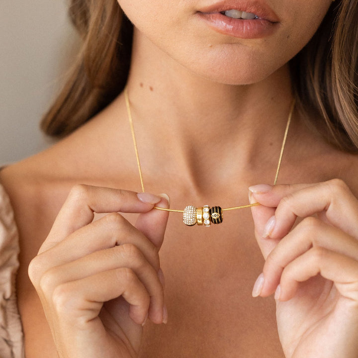Close-up of a person holding a gold necklace with a beaded pendant.