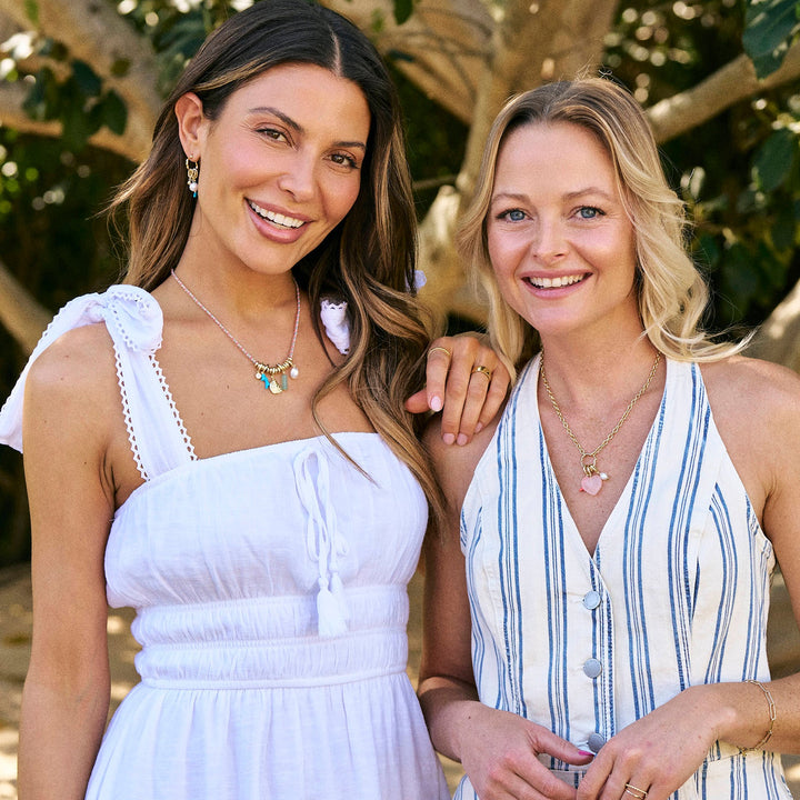 Two women standing together in a natural setting with trees and sand.