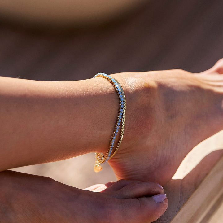 Close-up of a foot with a gold anklet on a wooden surface