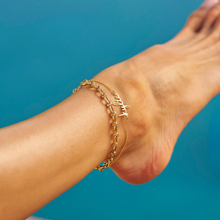 Close-up of a foot with gold anklets against a blue background