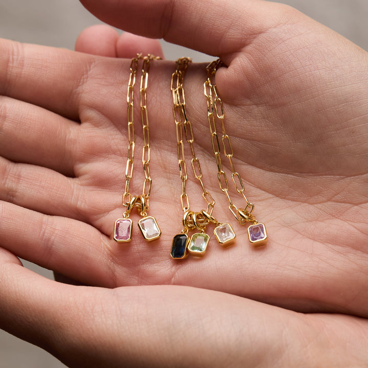 Gold necklaces with gemstone pendants held in a hand against a neutral background